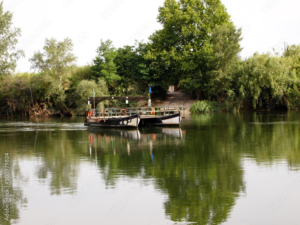 A river ferry consisting of two boats and a deck floats across a calm river. A river ferry consisting of two boats and a deck floats across a calm river.