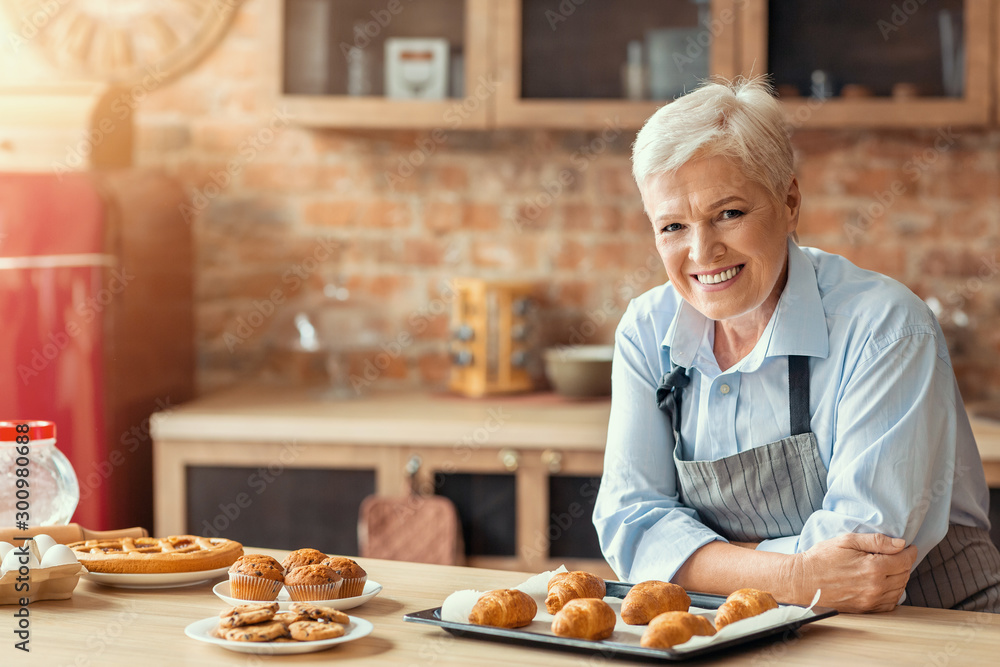 Smiling old lady posing with freshly baked pastry in kitchen