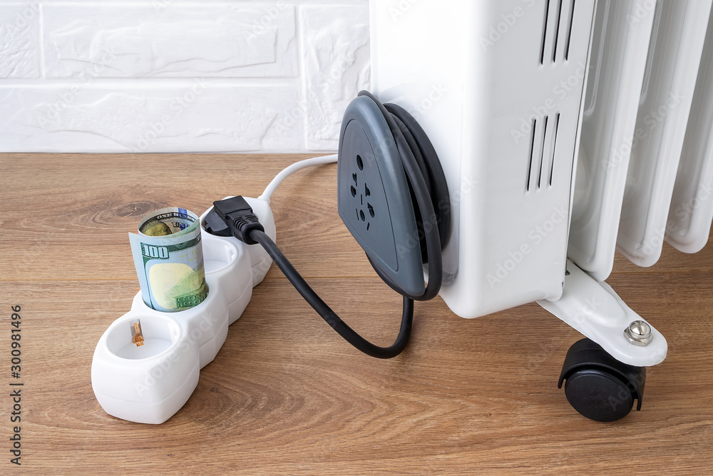 One hundred dollar bill inserted into extension cord near electric oil  heater plug. Expensive electricity and higher electricity costs during the  cold season concepts. Stock Photo | Adobe Stock