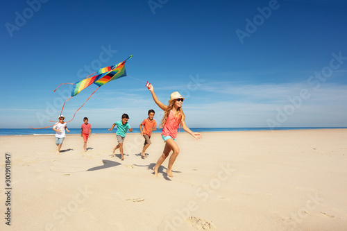 Girl run with kite and group of kids on the beach
