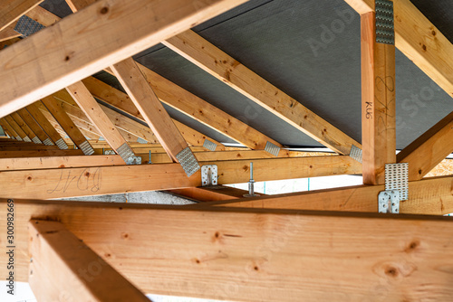 Roof trusses covered with a membrane on a detached house under construction, view from the inside, visible roof elements and truss plates.