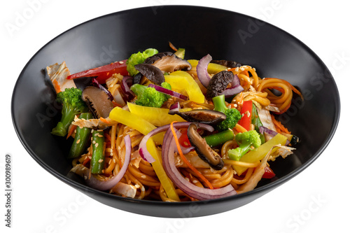 Sliced grilled vegetables, noodles in sauce, sesame seeds in a black plate isolated on white background, side view