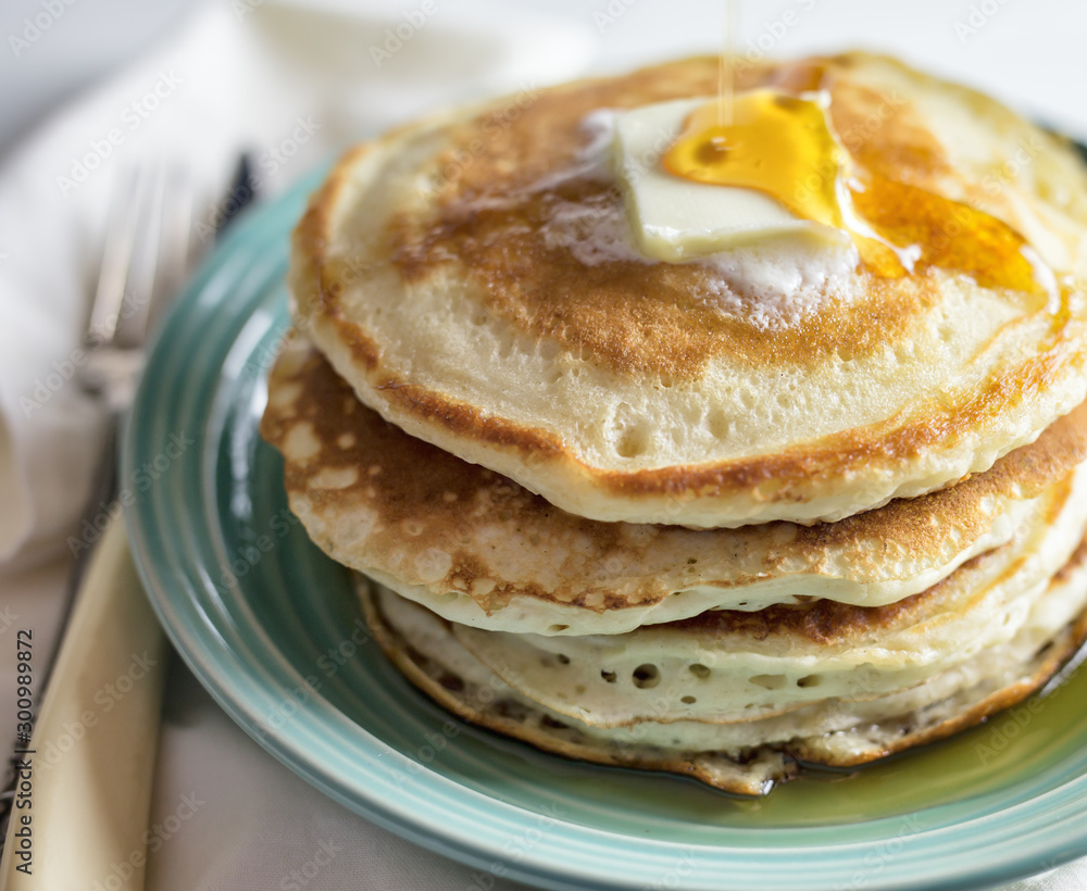 Syrup being poured on a stack of pancakes with butter on a blue plate. 