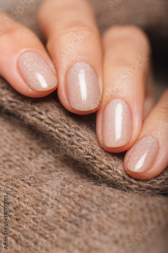 Nude color manicure on short round natural nails with brown knitted scarf