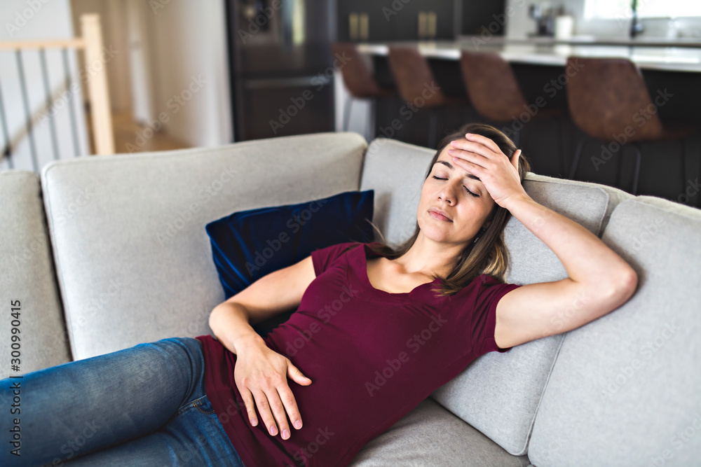Obraz premium A Sick woman lying on sofa in the living room with stomach ache