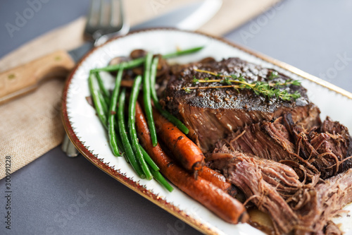 Slow cooked beef roast with carrots and green beans with thyme garnish. 