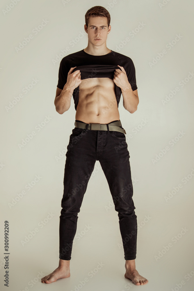 Muscle strong beautiful stripped male model in denim jeans and black t-shirt with belt on white isolated font background Muscle strong beautiful stripped male model in denim jeans and black t-shirt with belt on white isolated font background