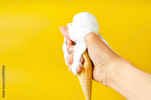 Creamy ice cream melted in the hands on a yellow background. The ice cream cone began to melt running down the arm.