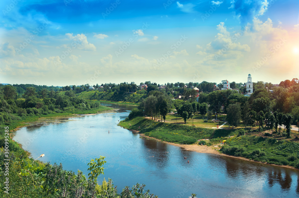 red church with blue domes from Rzhev town on the shore surrounded by green trees, view from Volga river at sunny summer day red church with blue domes from Rzhev town on the shore surrounded by green trees, view from Volga river at sunny summer day