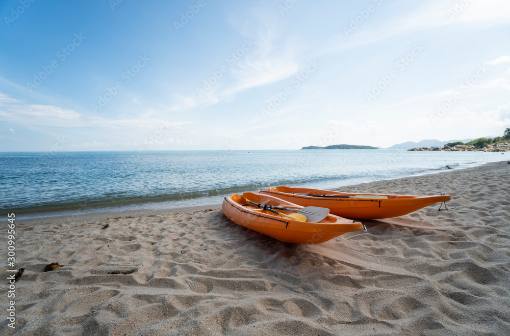 Fototapeta premium Two colorful orange kayaks on a sandy beach ready for paddlers in sunny day. Several orange recreational boats on the sand. Active tourism and water recreation.