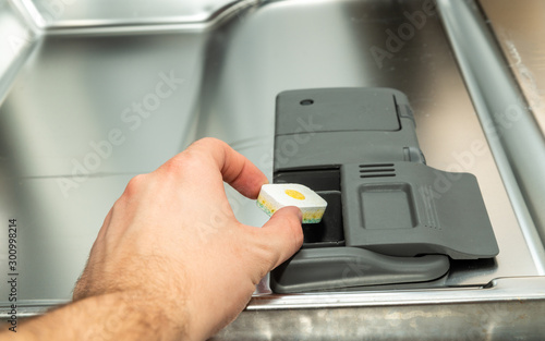 Loading the tablet into the dishwasher. The concept of using a dishwasher to wash dishes. A man puts the tablet in the dishwasher to wash dirty dishes.