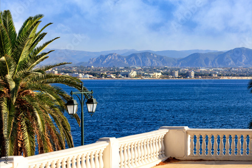 Beautiful seascape on the promenade  a street lamp under a palm tree looks at the sea  city and mountains in blur.