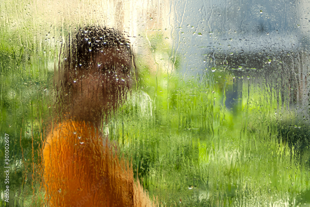 Fototapeta premium Blurred girl silhouette through wet window glass