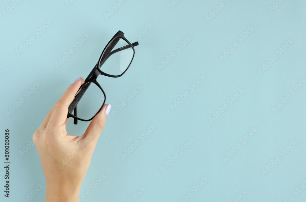 Hand with eyeglasses composition on blue background. - obrazy, fototapety, plakaty 