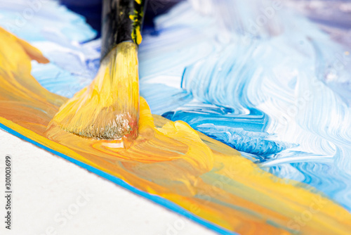 Yellow gouache paint and paint brush close up abstract background.