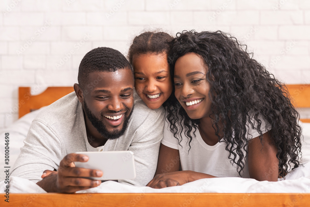 Obraz premium Happy afro man taking selfie with his wife and daughter
