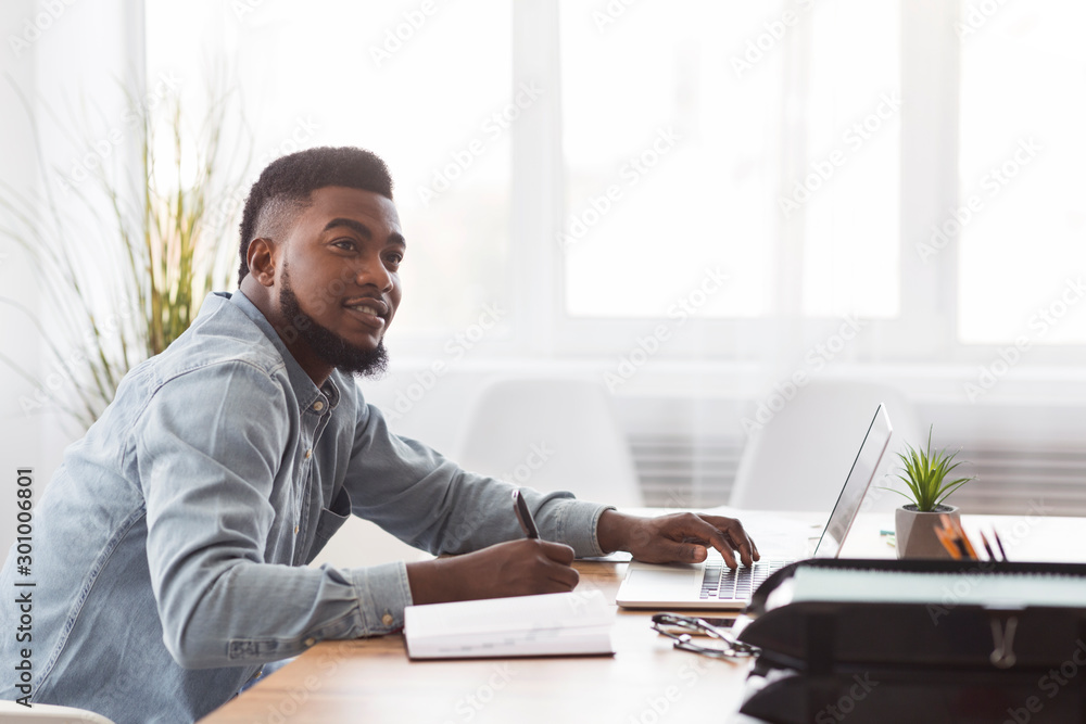 Black man taking notes from laptop at workplace in office Black man taking notes from laptop at workplace in office