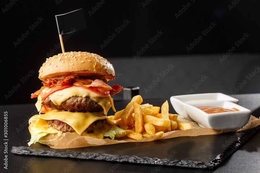 Big double cheeseburger with french fries isolated on black background. hamburger with beef patty , bacon, onion, tomato, lettuce pickles, aged cheddar, mustards, tomato jam, mayo. Horizontal