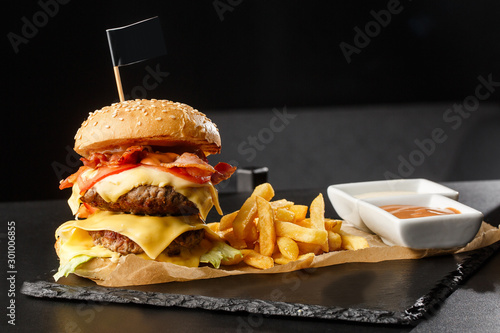 Obraz na płótnie Big double cheeseburger with french fries isolated on black background. hamburger with beef patty , bacon, onion, tomato, lettuce pickles, aged cheddar, mustards, tomato jam, mayo. Horizontal w salonie