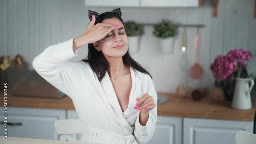 Portrait of woman in bathrobe applies cream on her face and does facial massage Portrait of woman in bathrobe applies cream on her face and does facial massage