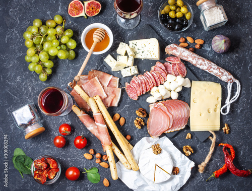Italian antipasto with prosciutto, ham, cheese, olives and grissini breadsticks on black stone background.