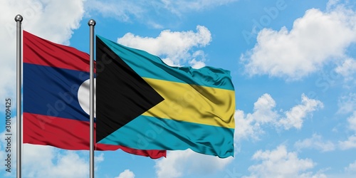 Laos and Bahamas flag waving in the wind against white cloudy blue sky together. Diplomacy concept, international relations.