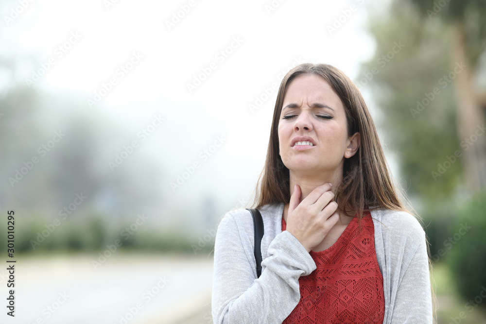 Ill woman suffering throat sore walks in a park a foggy day