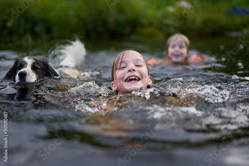 Two children and a dog swim in a river near the shore.  The mood of summer, warmth and joy from swimming.