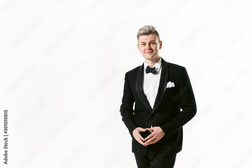 Portrait of young smiling handsome man in tuxedo stylish black suit, studio shot isolated on white background. Showman or toastmaster in jacket with bowtie Portrait of young smiling handsome man in tuxedo stylish black suit, studio shot isolated on white background. Showman or toastmaster in jacket with bowtie
