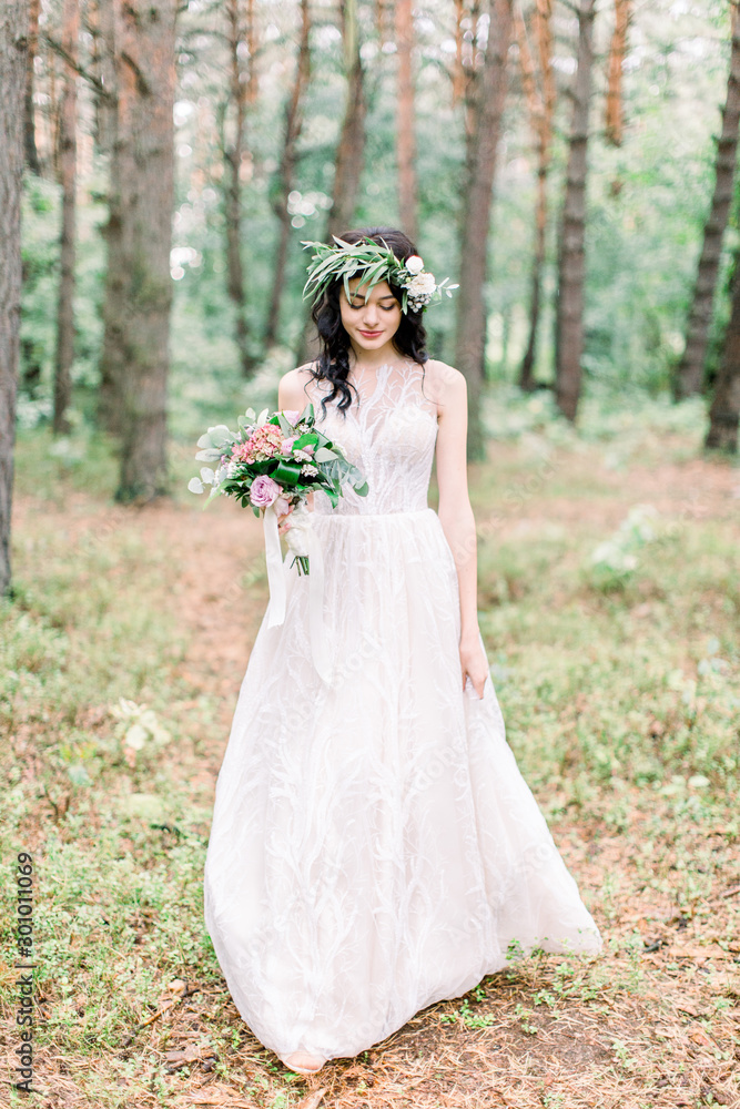 Full-length view of the smiling bride in the wedding dress walking in the green forest.