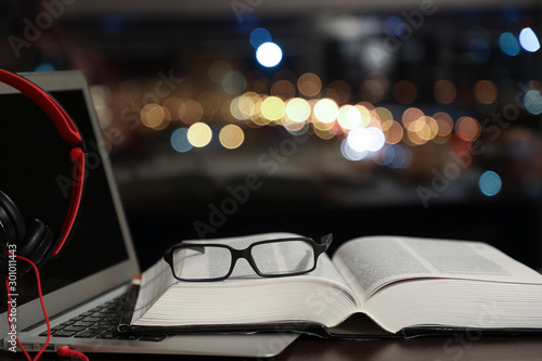 laptop with headphones and an open book with glasses, traditional reading and audiobook