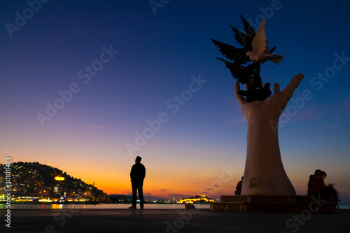 Hand Statue that represent Peace at sunset. Kusadasi is populer tourism destination in Turkey. Silhouette of a man is looking across. photo
