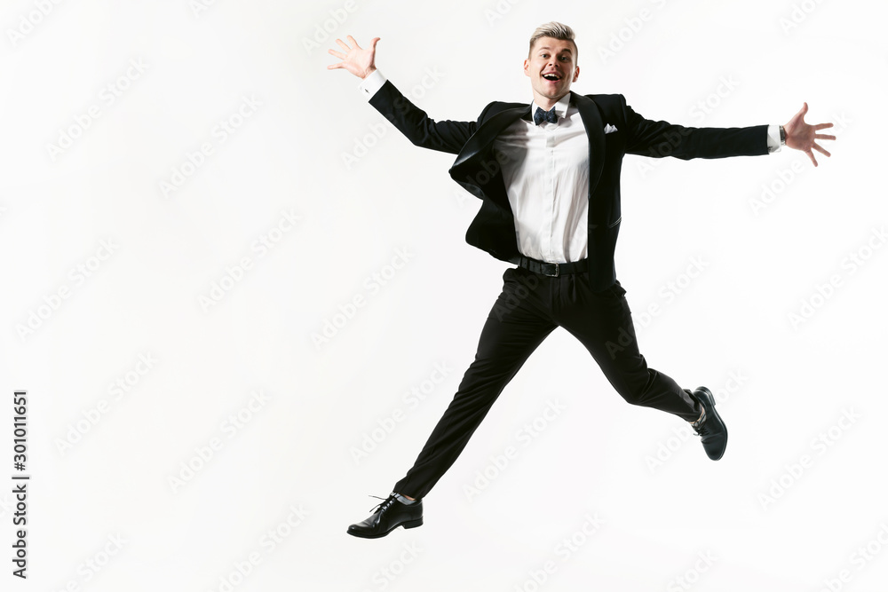 Portrait of young smiling handsome showman in tuxedo stylish black suit, studio shot jumping at white background. Businessman in jacket with bowtie Portrait of young smiling handsome showman in tuxedo stylish black suit, studio shot jumping at white background. Businessman in jacket with bowtie