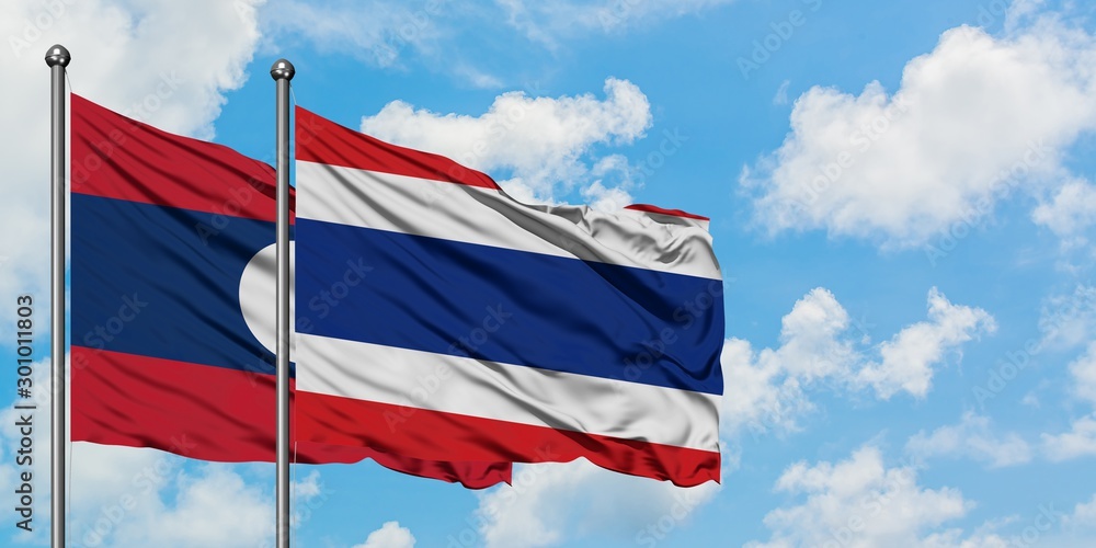 Laos and Thailand flag waving in the wind against white cloudy blue sky together. Diplomacy concept, international relations.