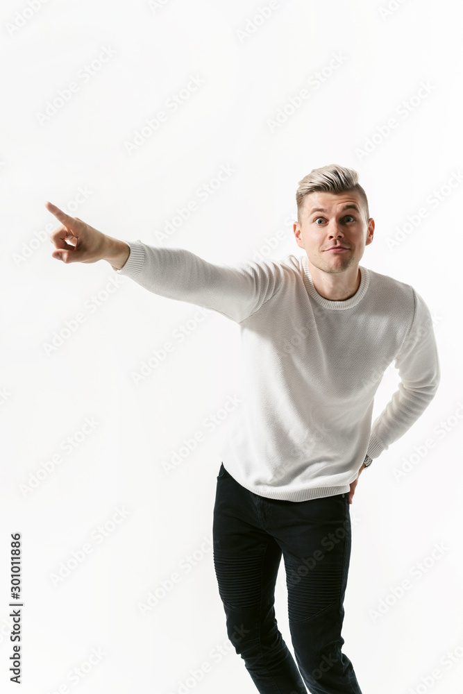 Portrait of handsome male student looking at camera over white background and showing emotions. Man points at copy space to the left side Portrait of handsome male student looking at camera over white background and showing emotions. Man points at copy space to the left side