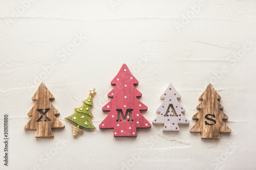 Four decorative wooden Christmas trees with carved letters xmas and christmas ornaments on a white textured background. Flat lay.