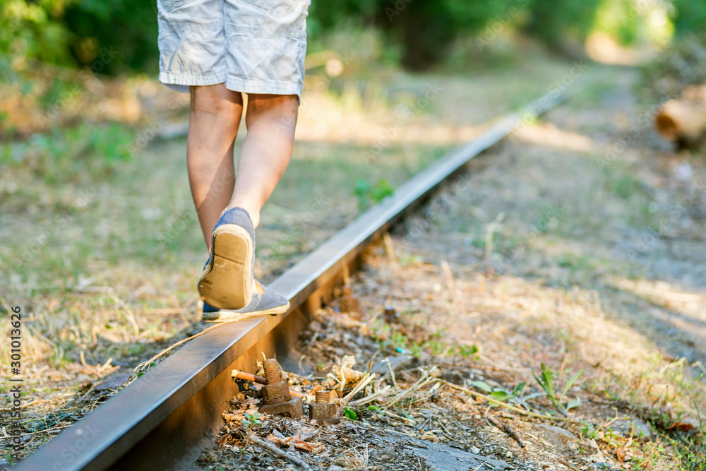 Little boy steps on the rails of the railway, being exposed to danger