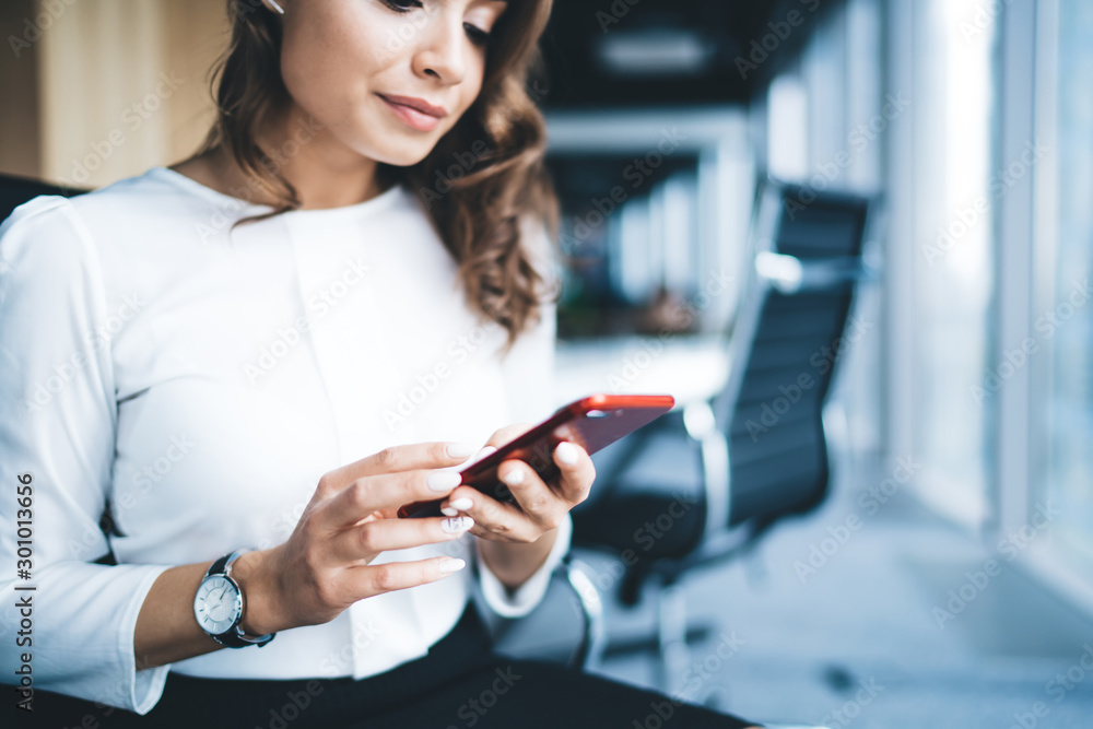 Modern amused female office worker using smartphone in office