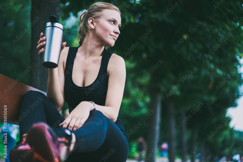 Charming good looking female runner resting on bench on urban setting after morning jogging around city, attractive sportswoman thoughtful looking away before starting hard workout on nature - obrazy, fototapety, plakaty 