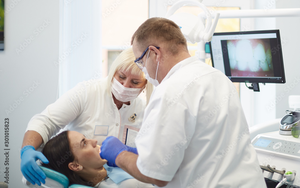 Obraz premium Doctor dentist treats teeth of a beautiful young girl patient. The girl on reception at the dentist. Doctor dentist treats tooth
