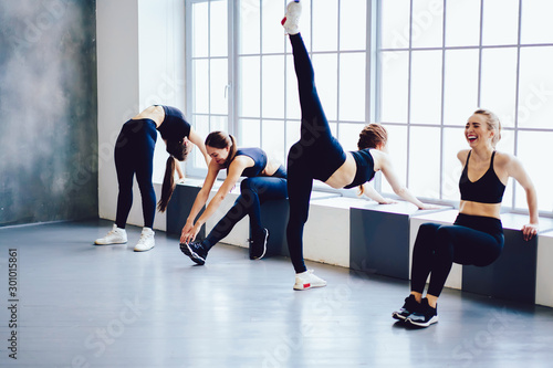 Successful thin women with strength bodies in tracksuits doing stretch before pilates exercises, group of cheerful girls enjoying time in studio club interior, healthy lifestyle and training concept