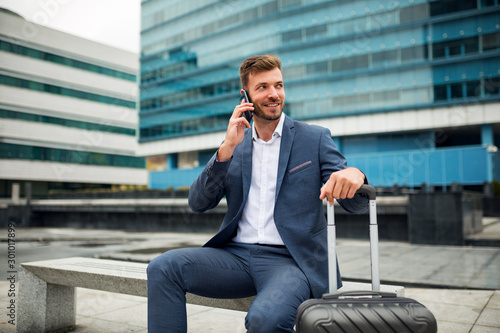 Smiling businessman with suitcase,talking on the phone