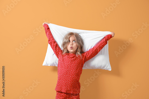 Surprised little girl in pajamas and with pillow on color background