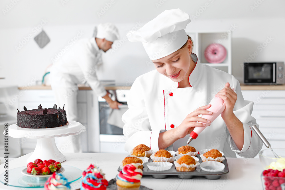 Female confectioner cooking tasty cupcakes in kitchen Female confectioner cooking tasty cupcakes in kitchen