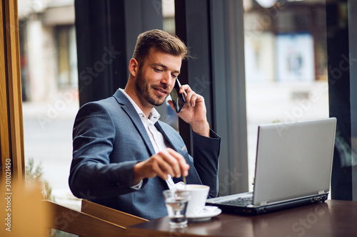 Young businessman in suit sitting in cafe bar and talking on the phone