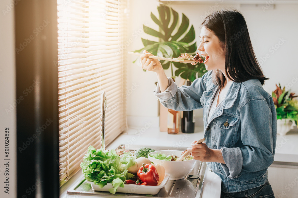 Happy woman eating healthy fresh vegetables salad in kitchen - obrazy, fototapety, plakaty 