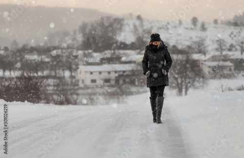 Woman in winter clothes walking on a road surrounded by snow and falling snow. Wintertime concept.