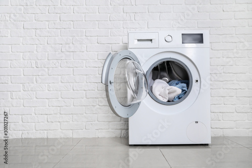 Modern washing machine with laundry near white brick wall photo