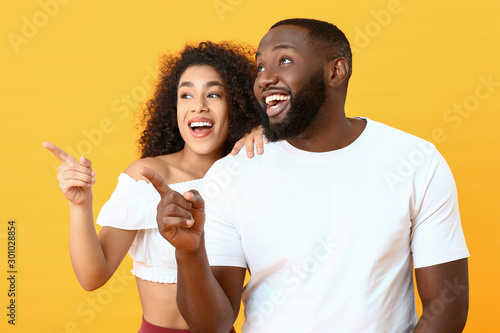 Portrait of happy African-American couple pointing at something on color background