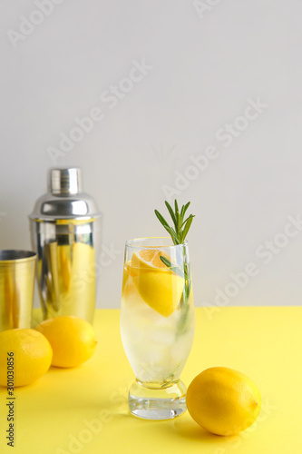 Glass of fresh lemonade and shaker on color table
